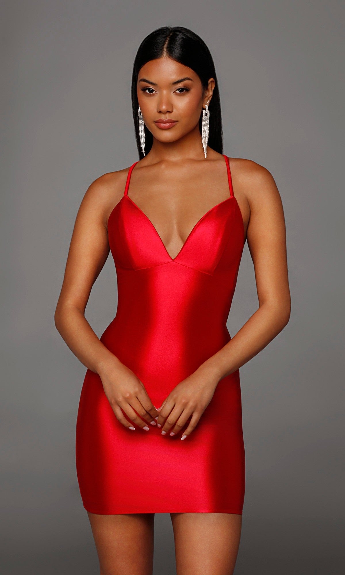 A woman poses against a plain gray background in a sleeveless, fitted red Alyce 40123 Lace-Up Short Satin Sheath Hoco Dress featuring thin straps and a deep neckline.
